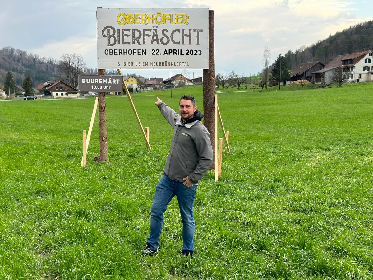 2023 fand das Bierfäscht Oberhofen zum erstenMal statt. (Archiv). Man sieht einen Mann vor einem grossen Schild, das auf einer grünen Wiese steht.