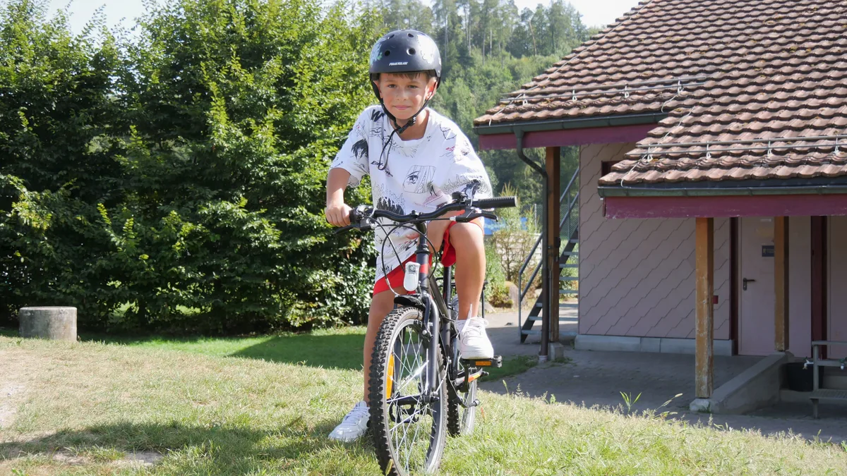 Man sieht einen Jungen auf einem Fahrrad. Er trägt einen Helm.
