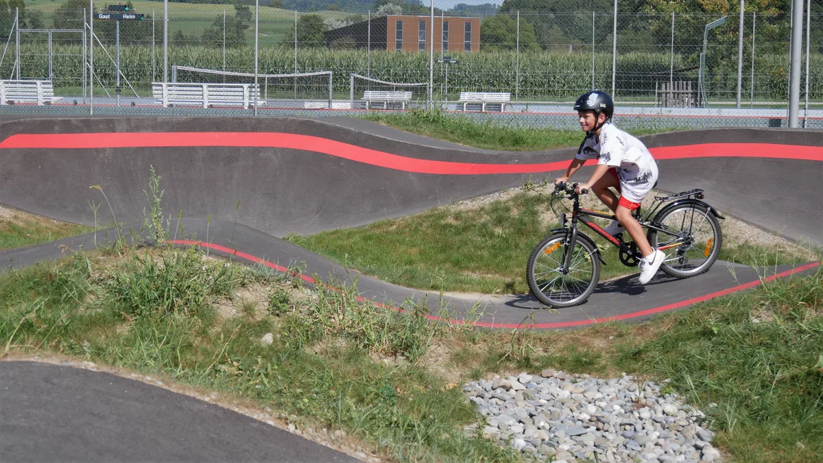Man sieht einen Jungen, der auf einem BMX-Rad durch einen Pumptrack fährt.