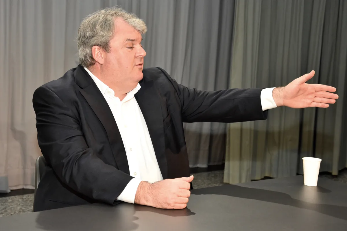 Ein korpulenter Mann gestikuliert an einem Tisch.