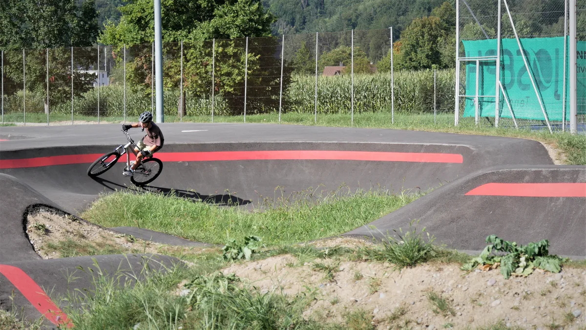 Man sieht einen Jungen, der auf einem BMX-Rad durch einen Pumptrack fährt.