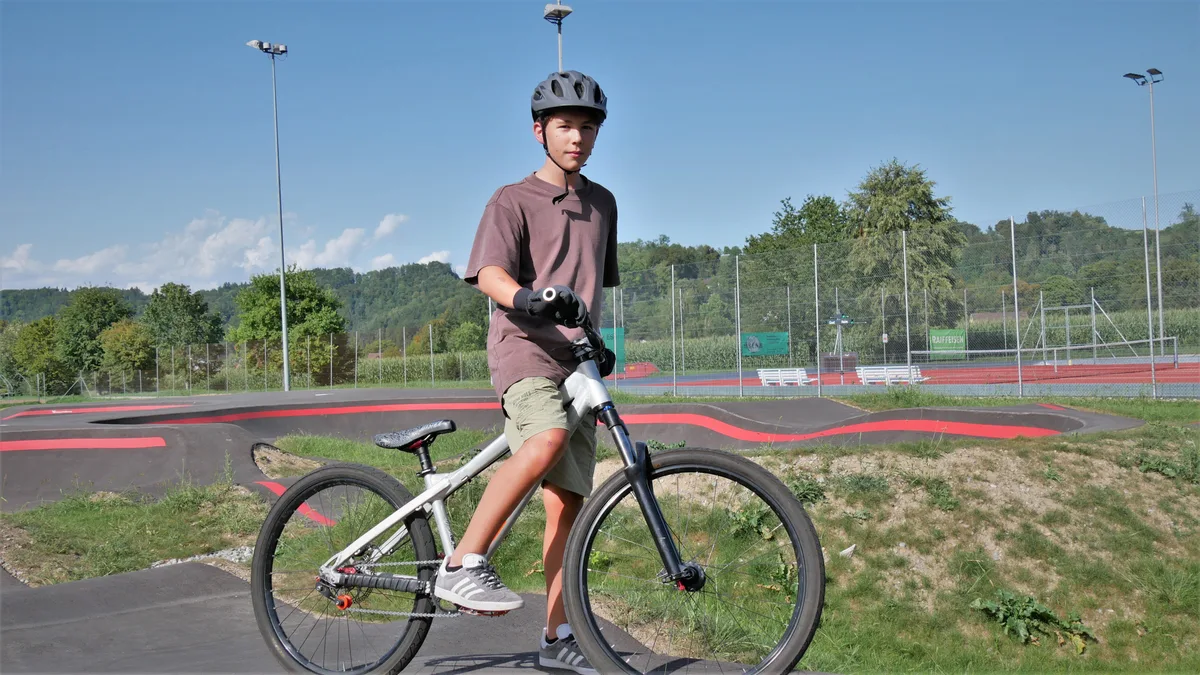 Man sieht einen Jungen auf einem Fahrrad. Er trägt einen Helm.
