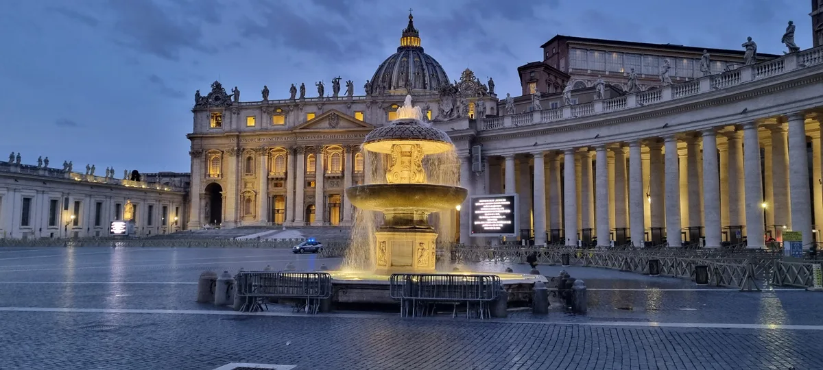 Man sieht den Petersplatz in Rom mit Brunnen und Petersdom.