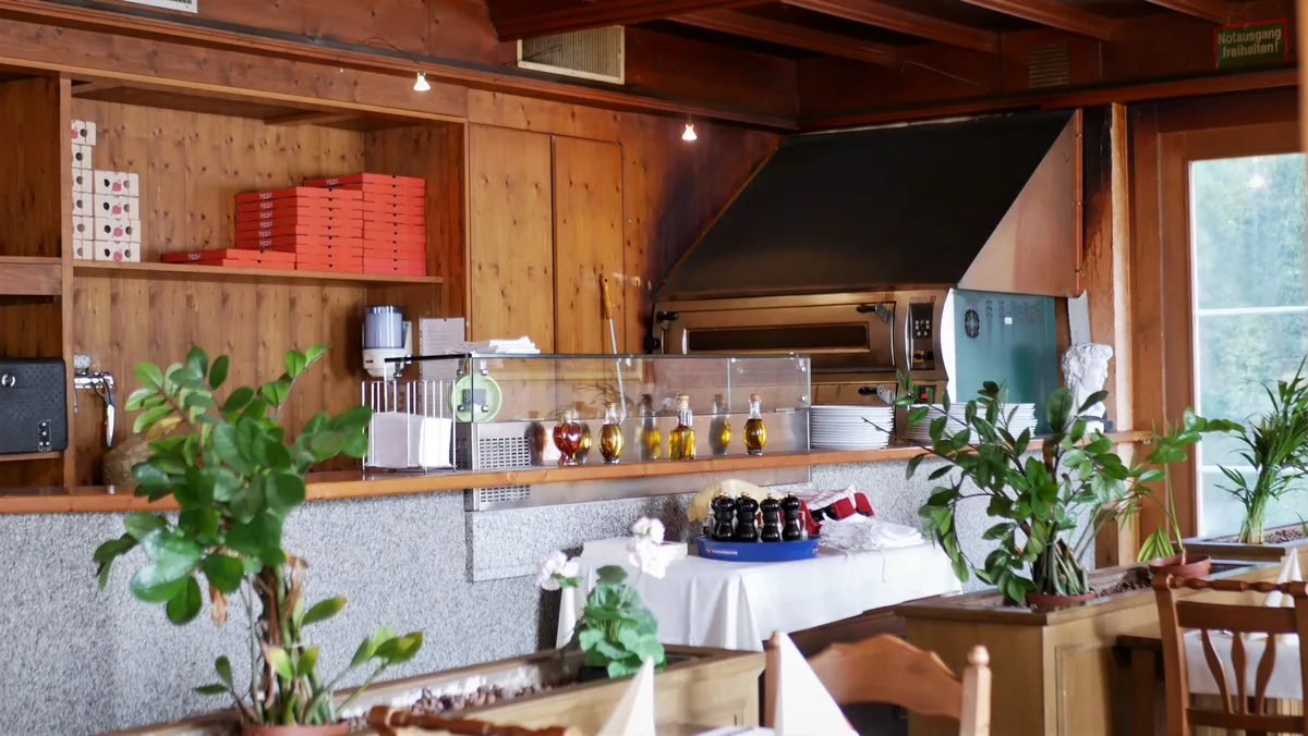 Man sieht eine Gaststube von Innen. Der Blick geht in die offene Küche mit Pizzaofen.