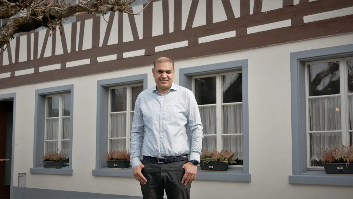 Man sieht einen Herrn mit einem blauen Hemd, der vor einem Restaurant steht.