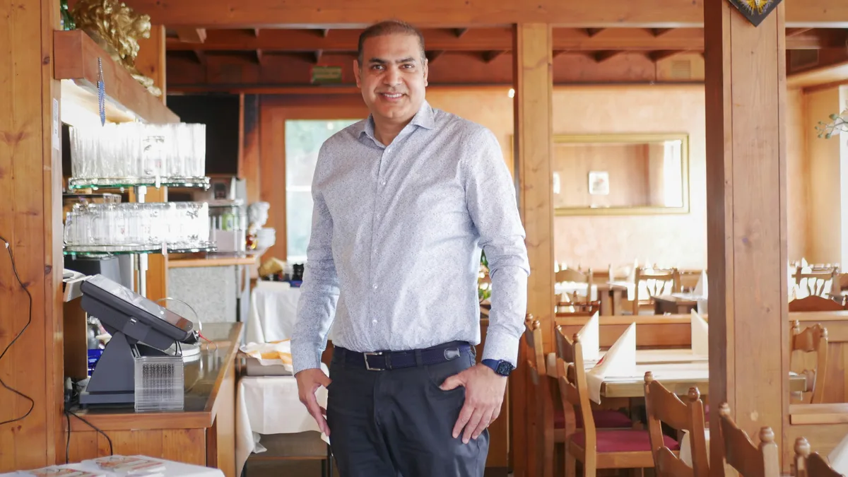 Man sieht einen Herrn mit einem blauen Hemd, der in einem Restaurant steht.