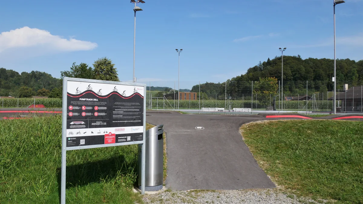 Man sieht eine Hinweistafel, die neben dem Startpunkt einer Pumptrack-Anlage steht.