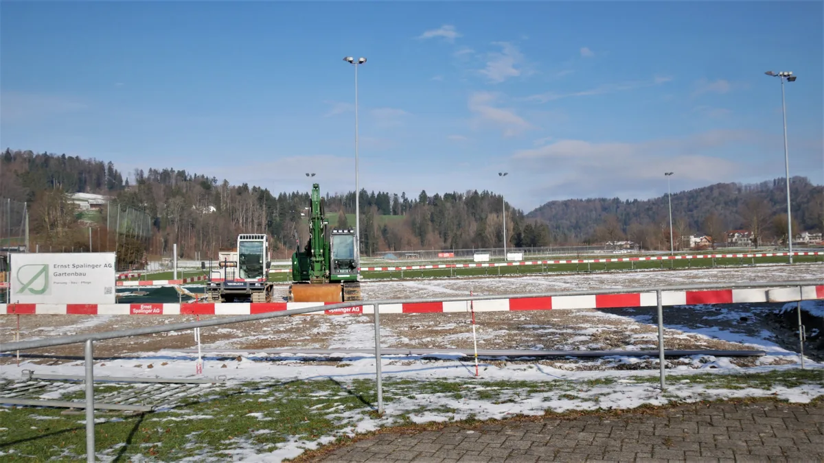 Man sieht eine Baustelle mit rot-weissen Abschrankungen, zwei Baggern und der Baugrube.