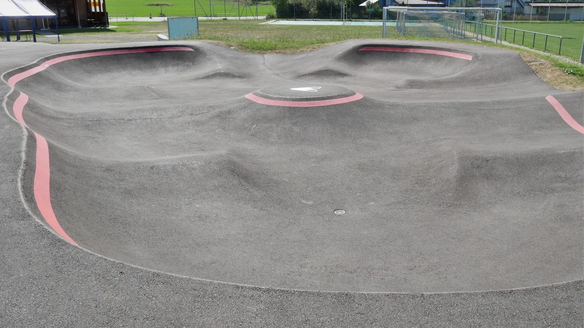 Es ist eine asphaltierte Pumptrack-Strecke mit farbigen Markierungen zu sehen.
