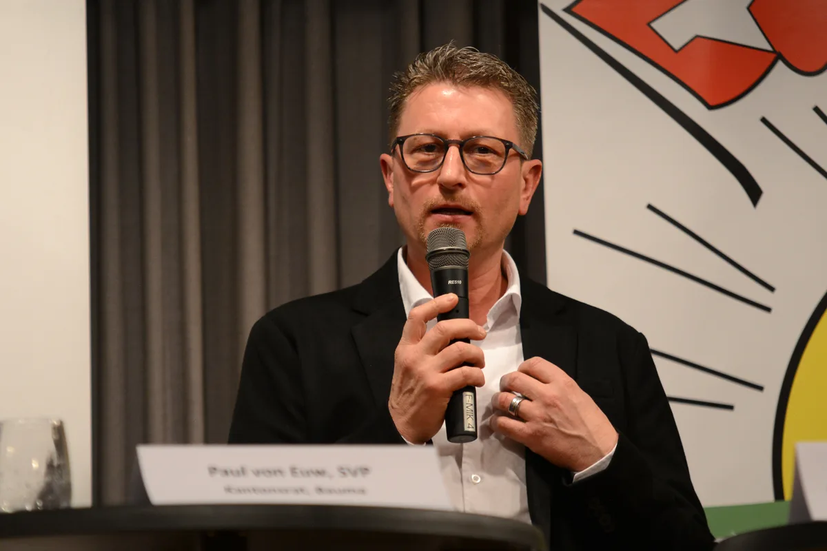 Ein Mann mit Brille bei einem Podiumsgespräch am Mikrofon.