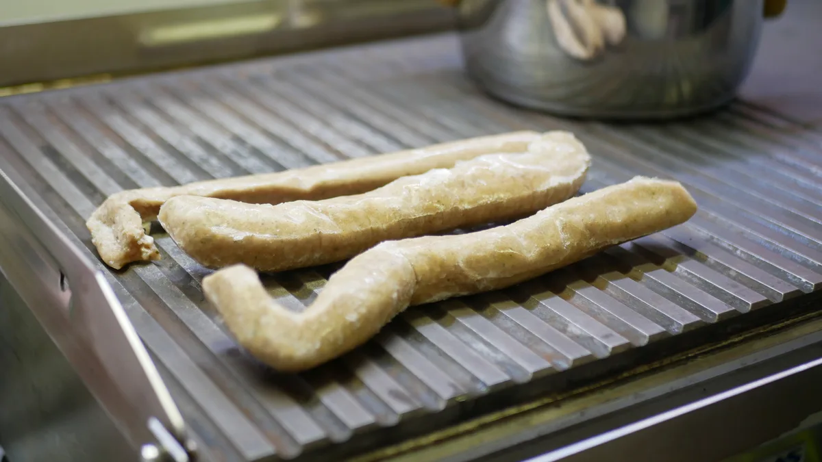 Man sieht halbwegs gefrorene Rostbratwürste Thüringer Art auf einem Grillrost.