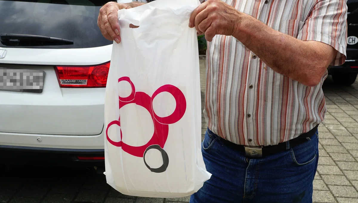 Ihre Akten erhalten sie dann in einem Plastiksack. Ein Patient hält einen Plastiksack hoch.