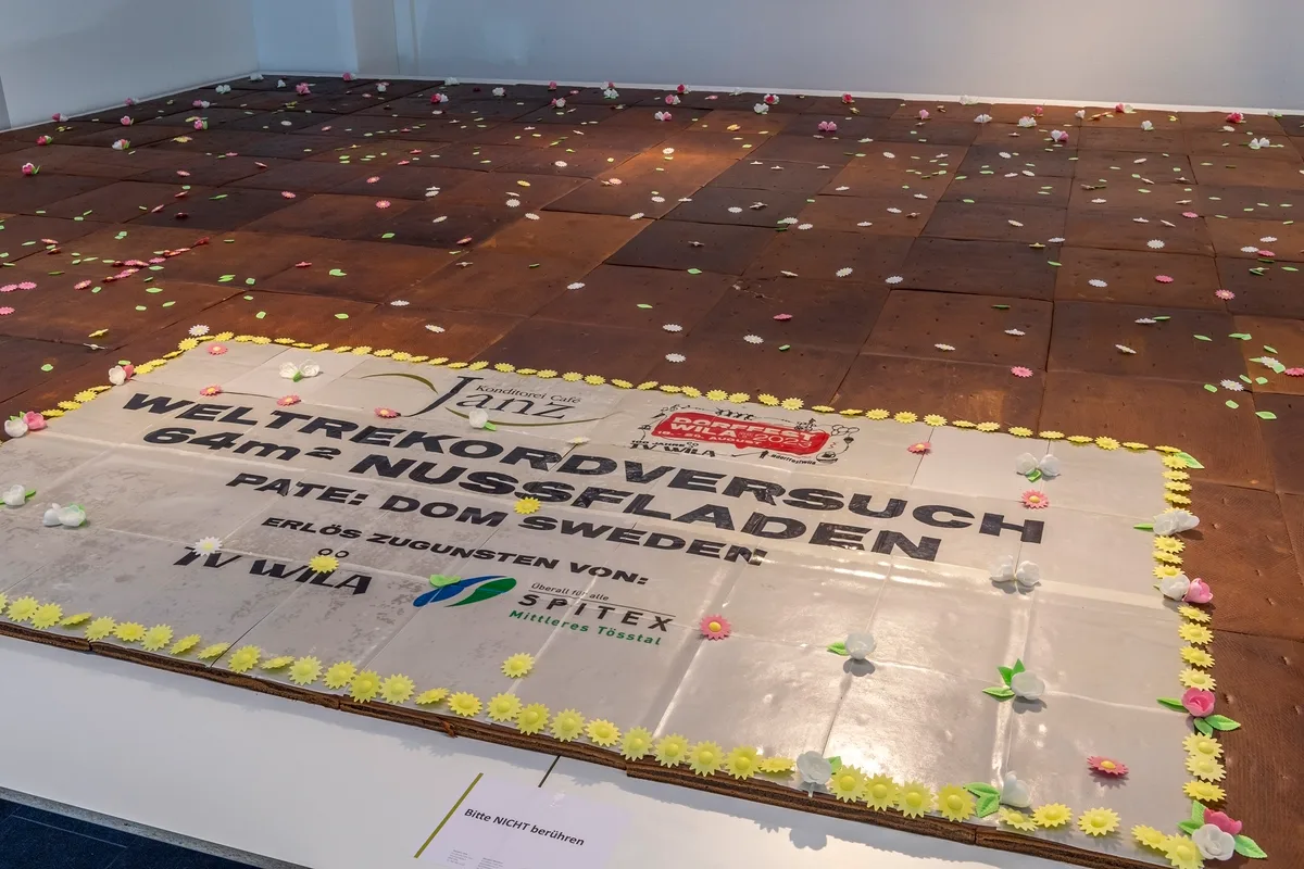 Die Aufschrift stimmt nicht ganz: Der Fladen war 38 Quadratmeter gross. Aber: Der grösste Nussfladen der Welt kommt trotzdem aus Wila. Grosser Fladen mit Aufschrift.