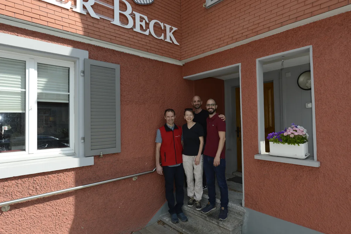 Vier Leute stehen im Eingang eines Gebäudes mit roter Fassade.