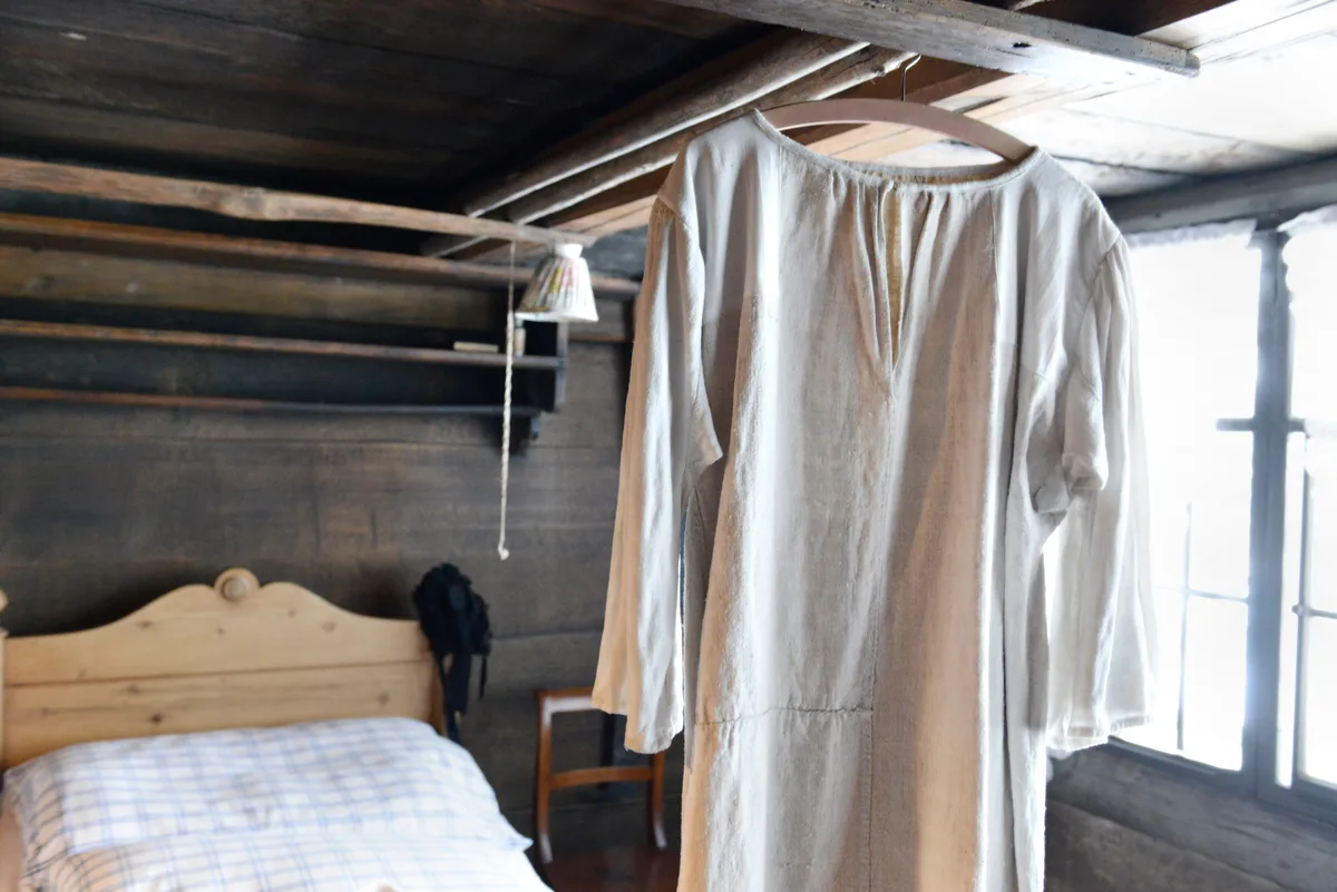 Man sieht ein altes Nachthemd, das über einem Bett hängt.