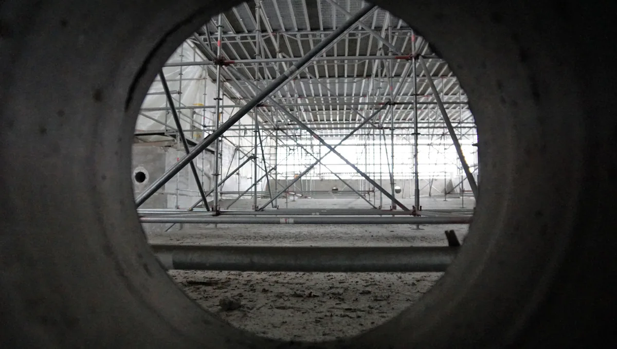 Man sieht durch eine runde Luke in die Baustelle des Hallenbadbeckens.