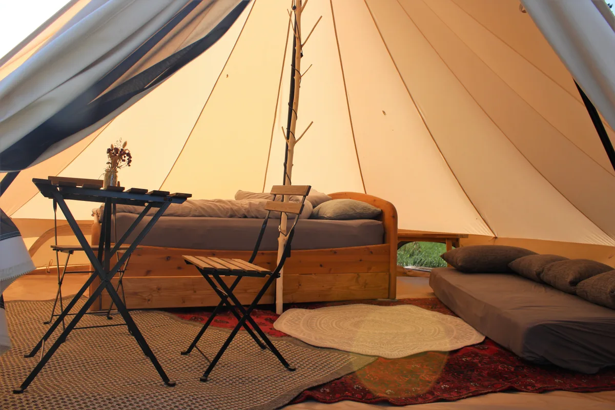 Auf dem Foto sieht man das Innere eines Zelts. Man erkennt einen Tisch und einen Stuhl sowie ein Bett.