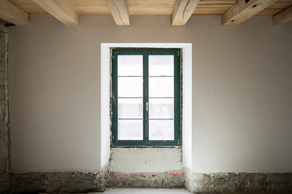 Man sieht ein grünes Fenster in einer weissen Wand.