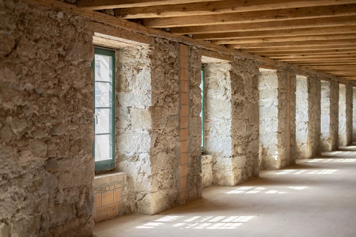Man sieht eine Fensterfront in einer Bruchsteinmauer ohne Verputz.