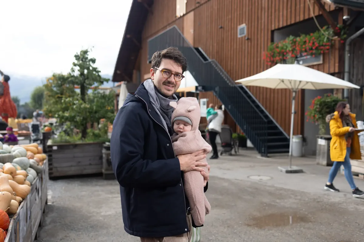 Ein Mann hält sein Kind in den Armen und lächelt in die Kamera.