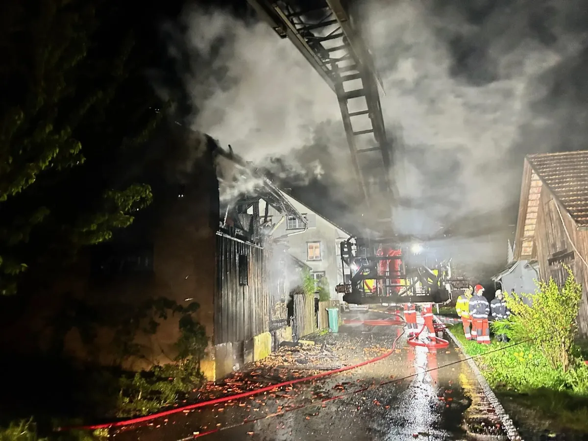 Man sieht eine Rauchwolke im Dunkeln und ein paar Feuerwehrleute in der Distanz.