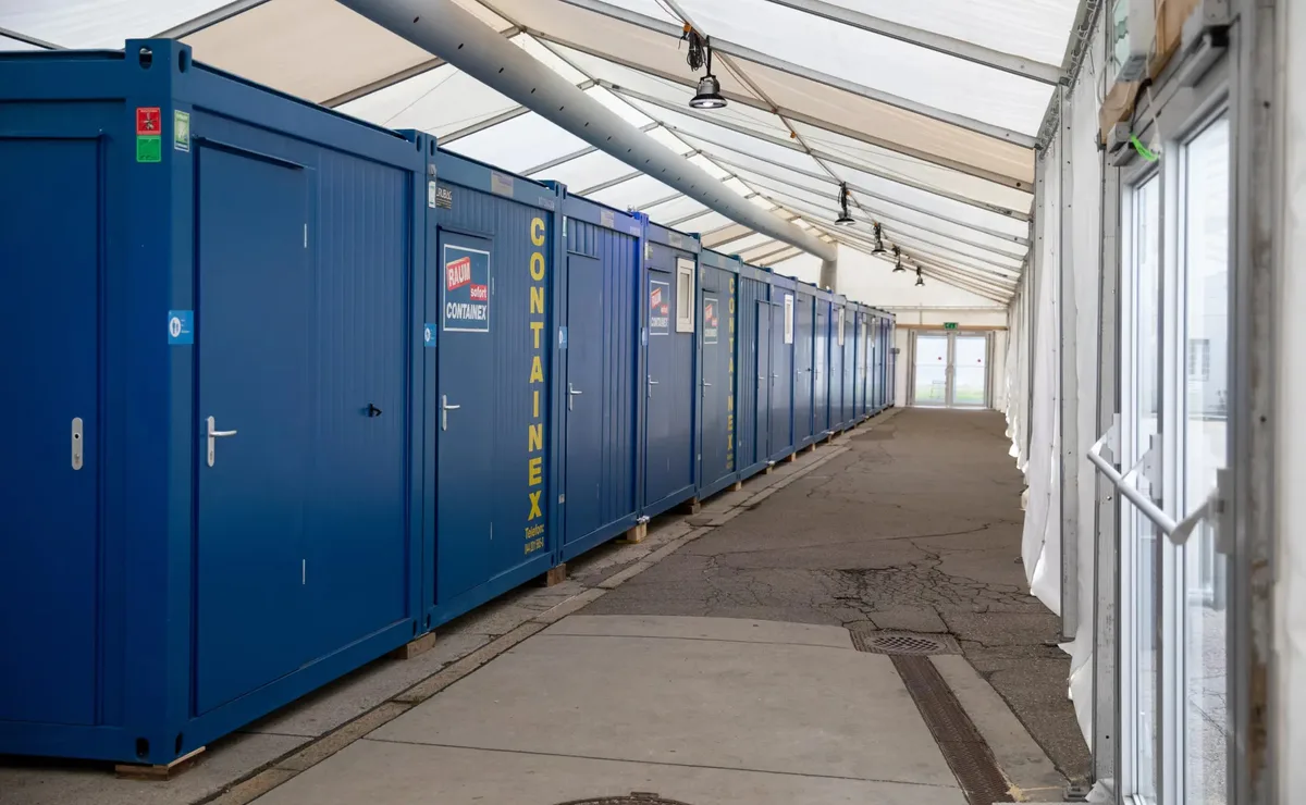 Man sieht mehrere blaue Container unter einem Zelt.
