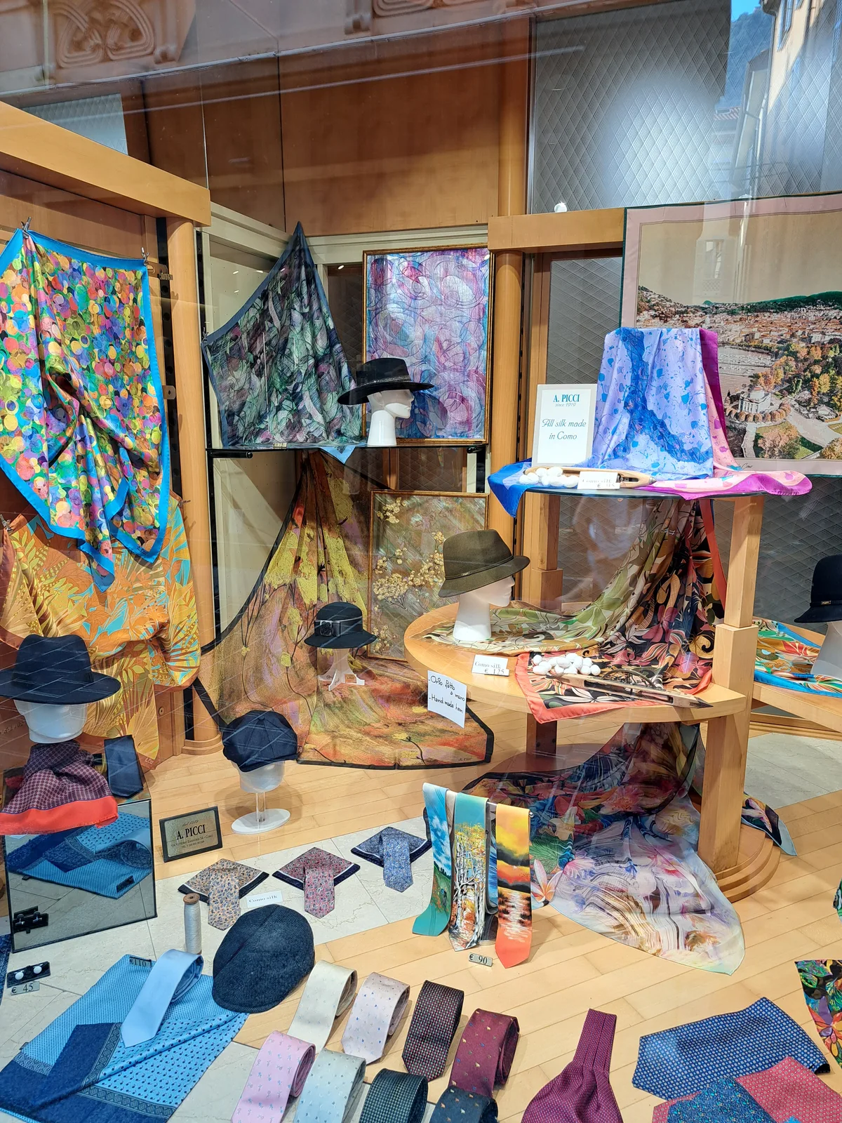 «All silk made in Como» – in einer Schaufensterauslage wirbt ein lokaler Seidenproduzent für seine Produkte. Ein Schaufenster mit Tüchern und Hüten