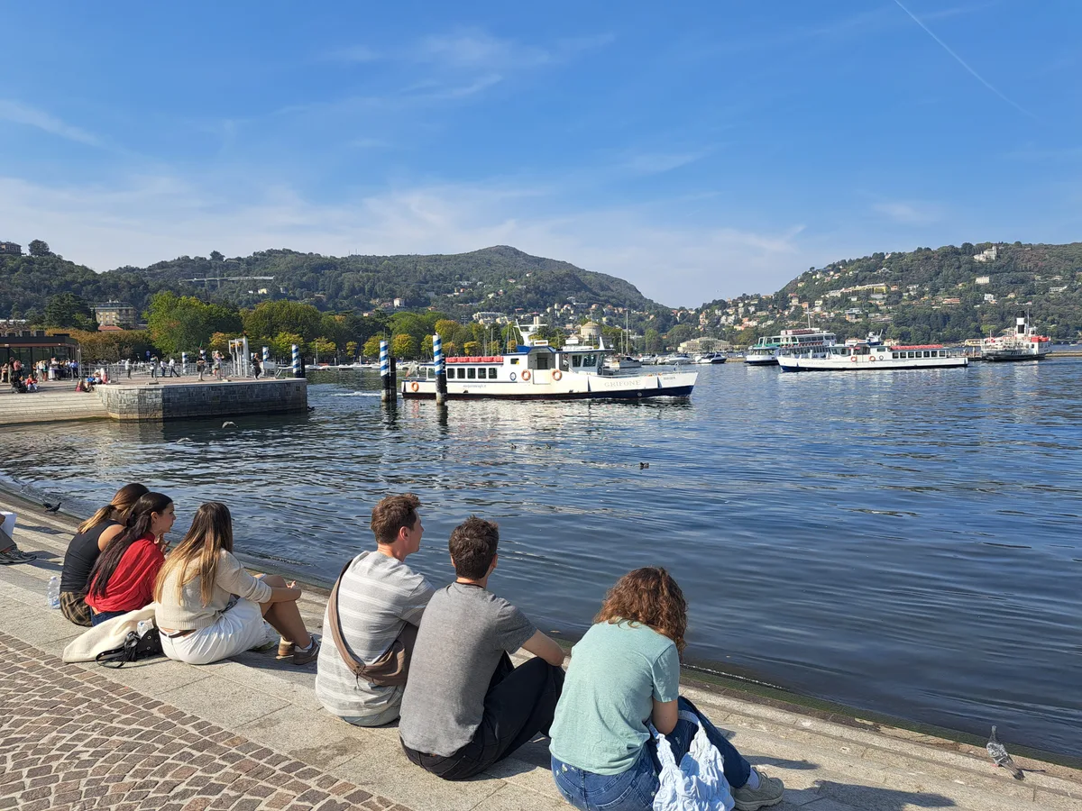 Wem der Rummel zu viel wird, findet am See ein paar Schritte weiter ruhige Plätzchen. Menschen sitzen am See und sehen den Booten zu.