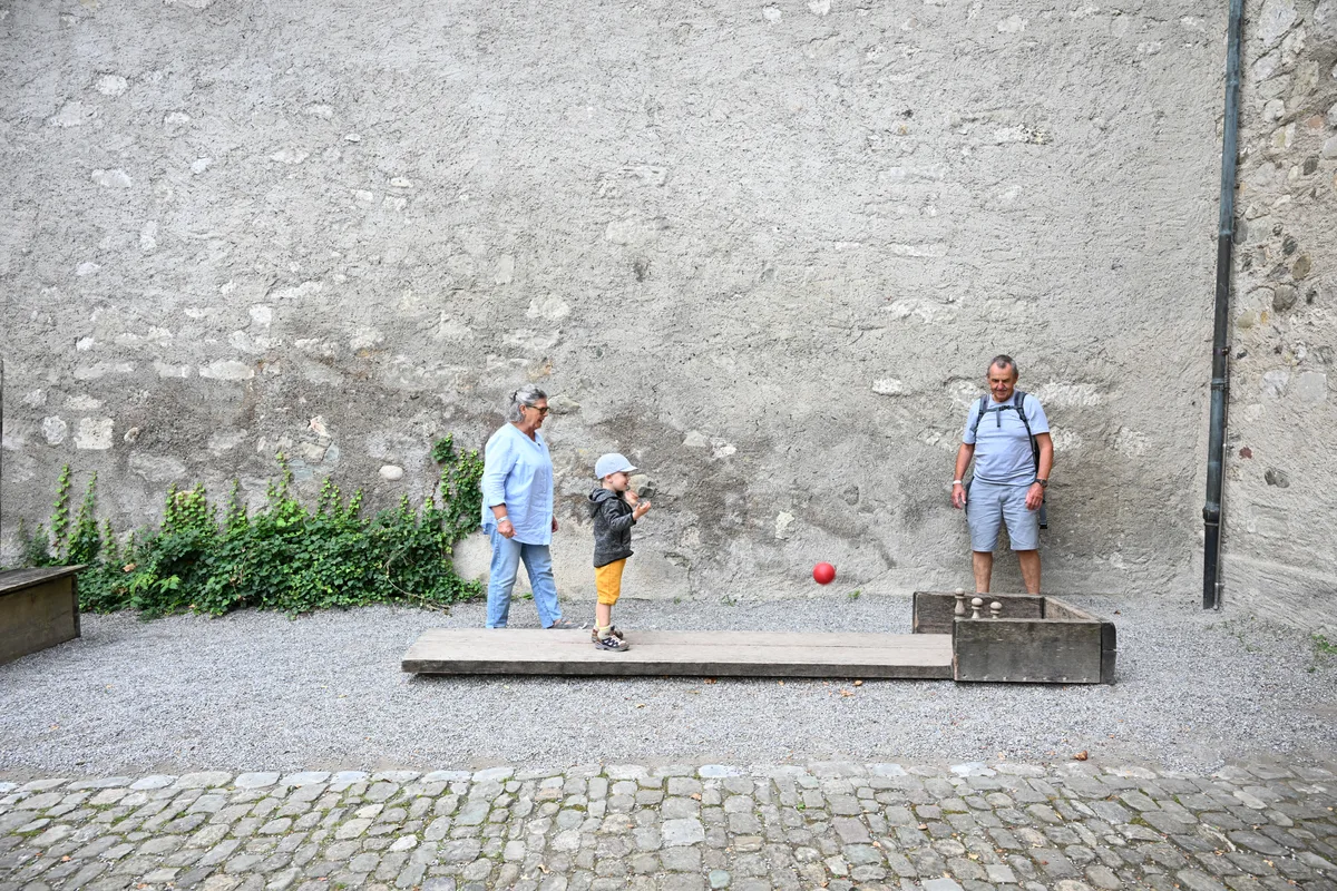 Man sieht zwei Erwachsene, die mit einem Kind vor einer Burg spielen.
