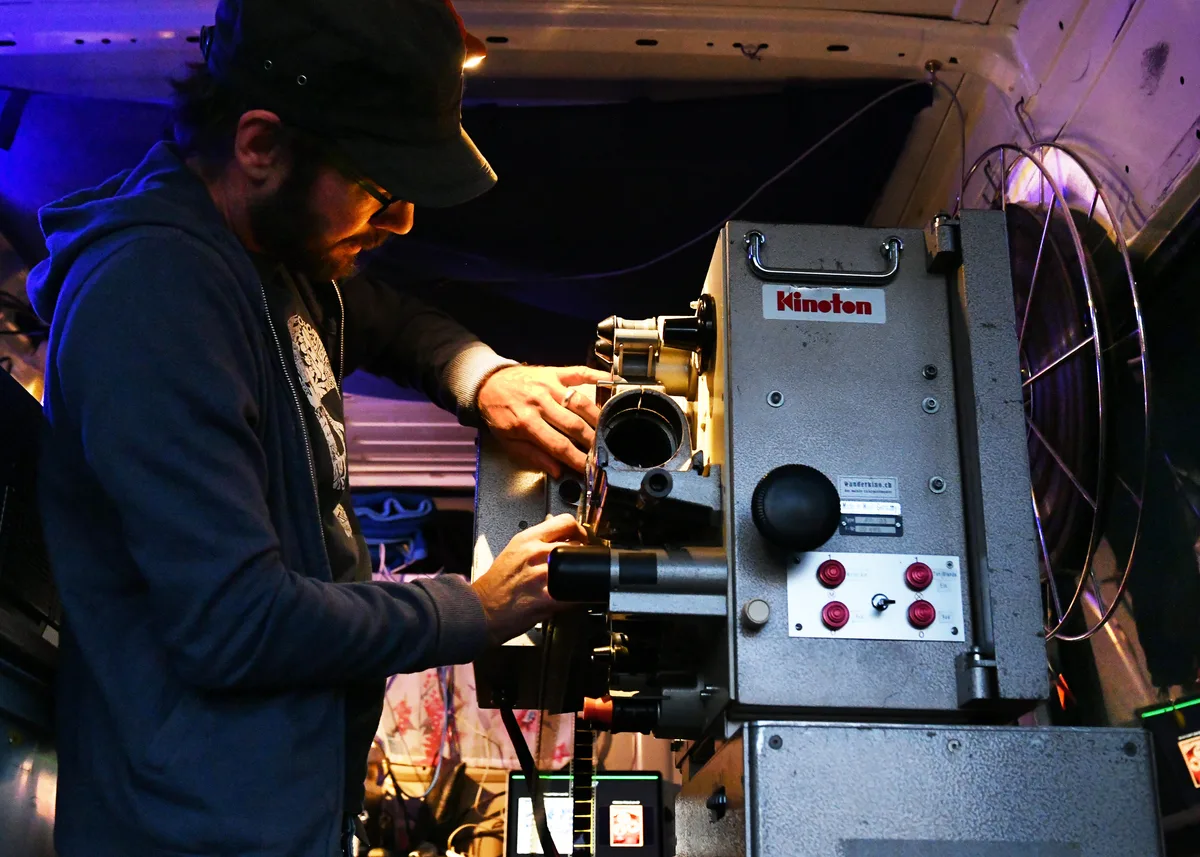 Man sieht einen Mann mit Baseballmütze, der einen analogen Kinoprojektor bedient.