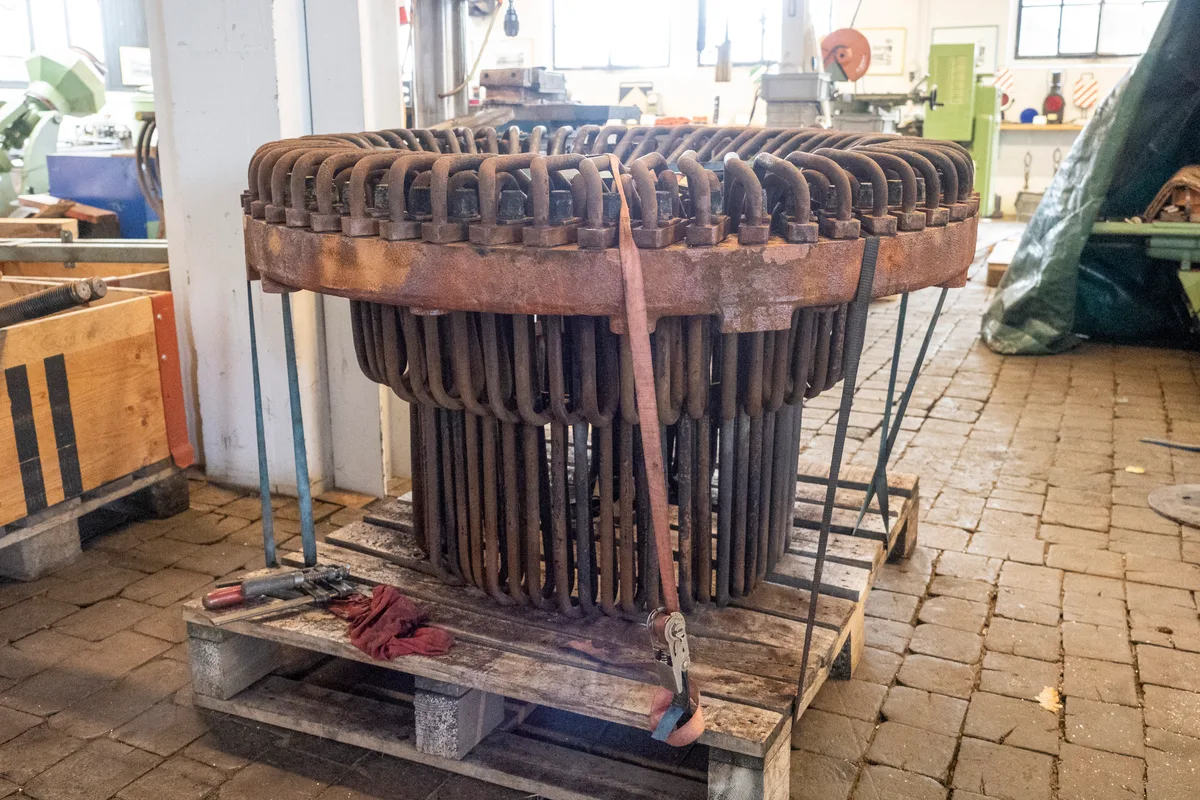 Das Sorgenkind: Der ausgebaute Überhitzer steht im Nebenraum und wartet auf seine Revision. Man sieht einen aus vielen Rohren zusammengesetzten Überhitzer, der auf einem Holzpalett steht.