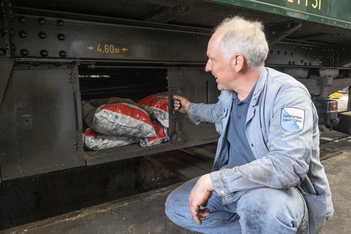Den alten Gefiederkasten unten am Fahrzeug nutzt die Dampfgruppe heute, um Kohle zu transportieren. Man sieht einen Mann, der neben dem Fahrzeug kniet und eine kleine Tür aufhält.
