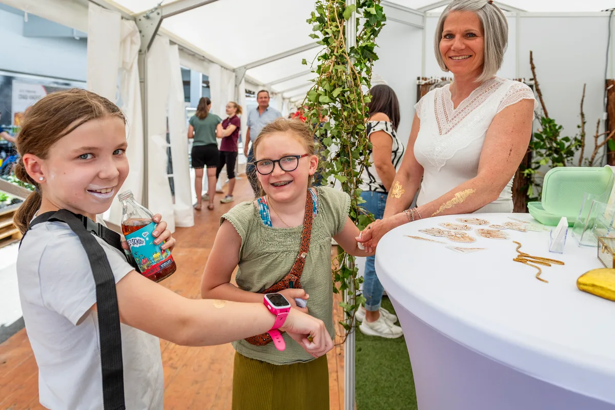 Luana und Elea lassen sich am Stand der DB-Hypnosetherapie ein goldenes Tattoo verpassen, ganz ohne Hypnose. Zwei Mädchen mit Gold-Tattoo.