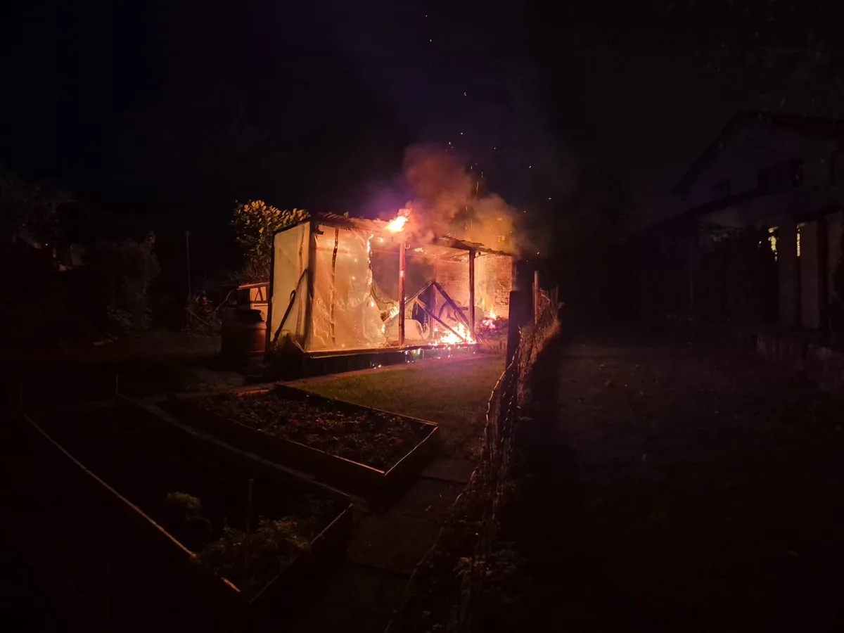 Der Bau aus Holz wurde bei dem Brand stark in Mitleidenschaft gezogen. Feuerwehrleute löschen eine brennende Gartenlaube.
