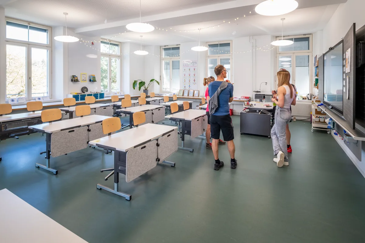 Auch im Altbau A, der aus dem vorletzten Jahrhundert stammt, wurde investiert und modernisiert. Das Innere eines neuen Schulzimmers mit ein paar Personen.
