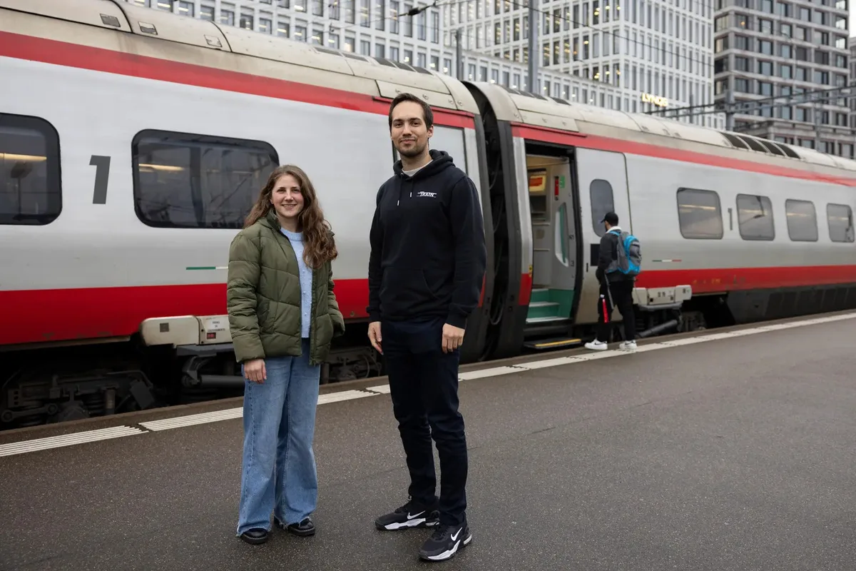 Man sieht zwei Menschen an einem Bahnhof.
