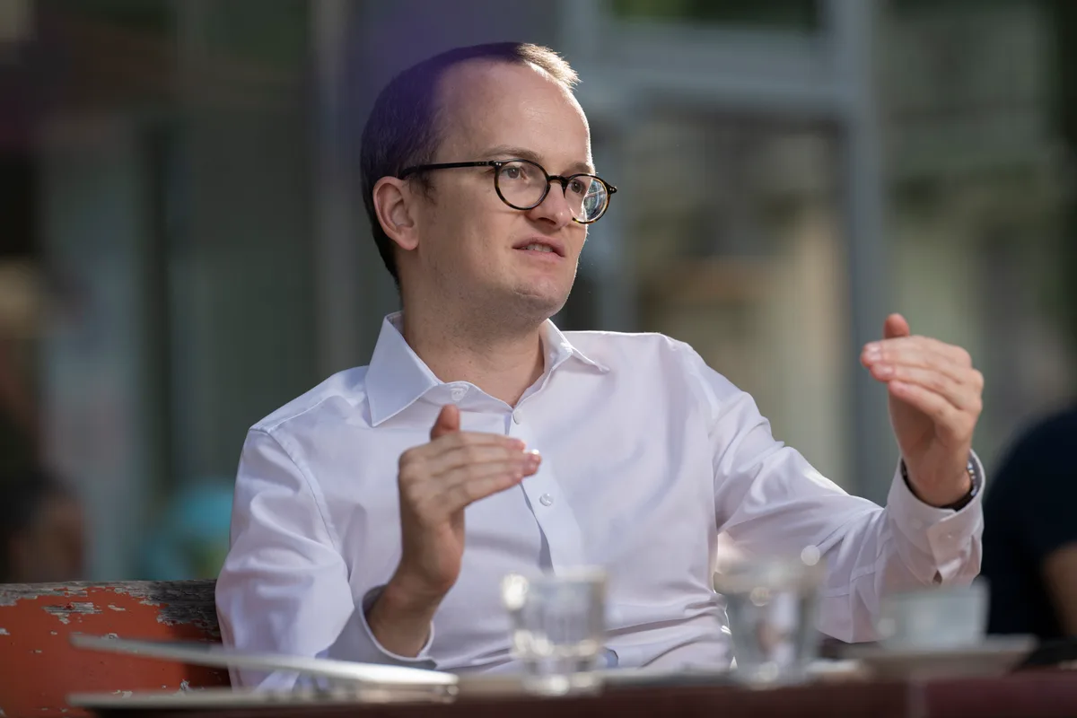 Man sieht einen Politiker mit einem weissen Hemd, der an einem Restauranttisch sitzt und wild gestikuliert.