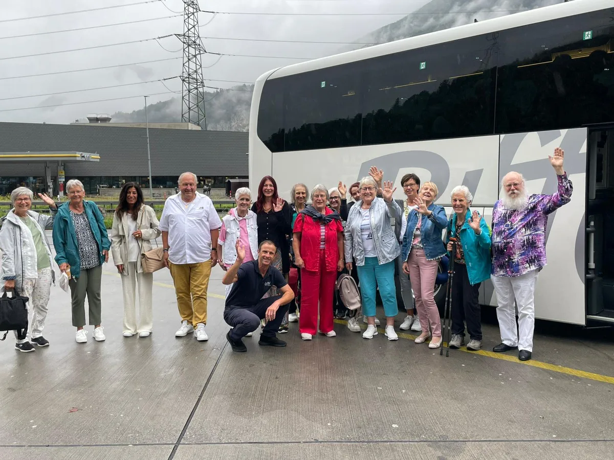 Eine Personengruppe steht winkend vor einem Bus.