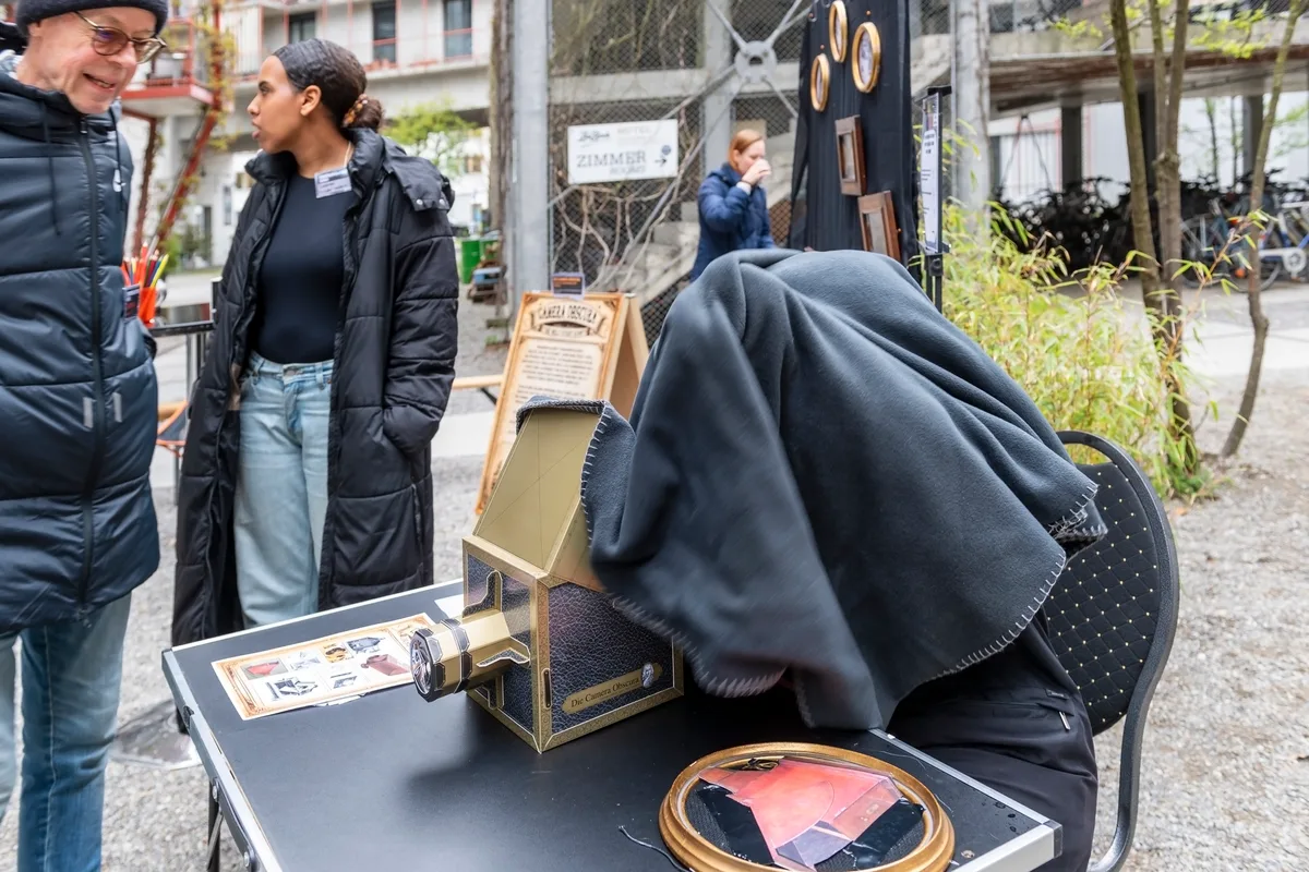 Eine Frau unter einem Tuch, hinter einer Camera Obscura.