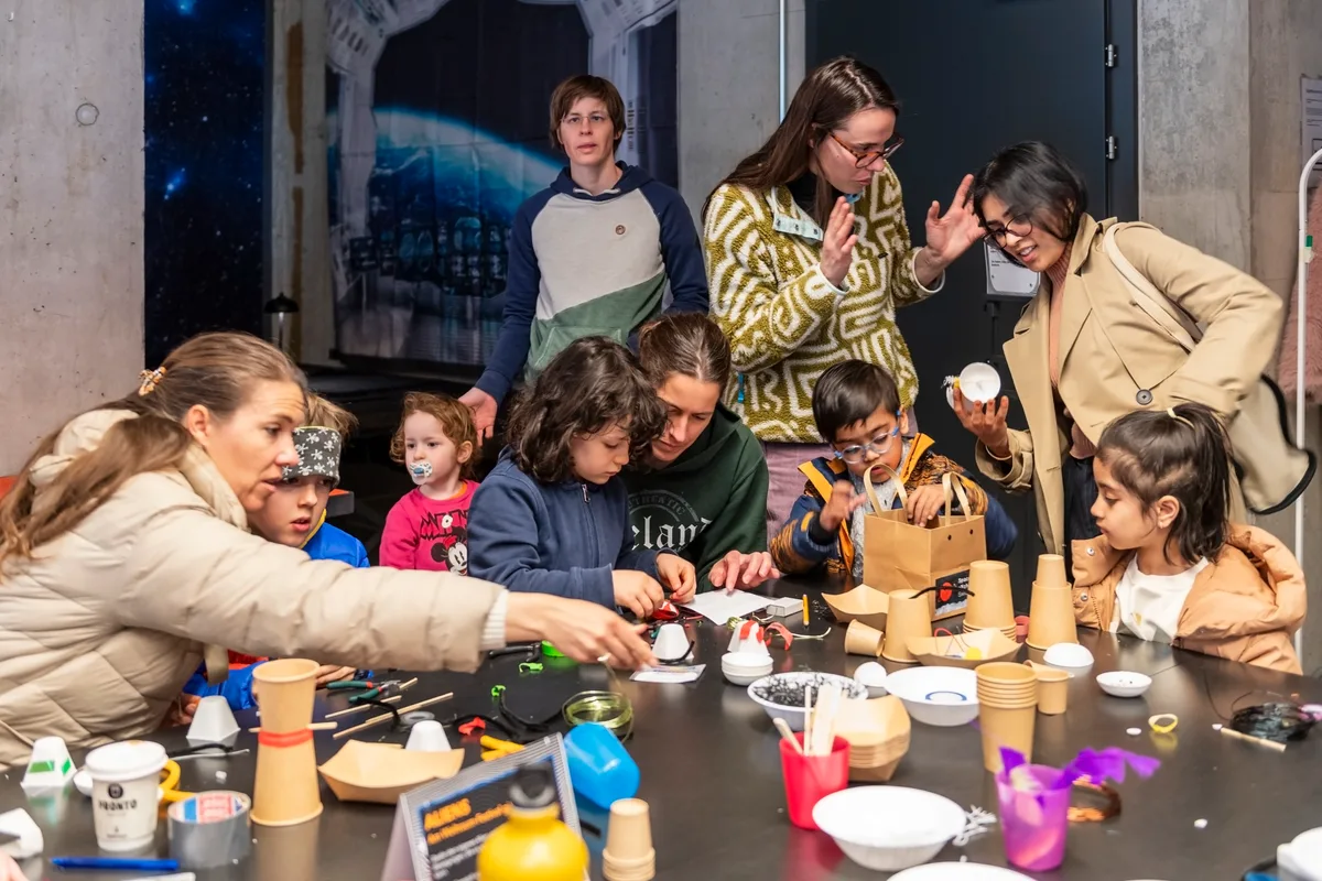 Kinder sitzen an einem Tisch und basteln etwas aus Kafibechern.