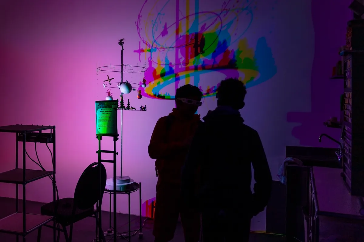 Ein pinker abgedunkelter Raum, man sieht ein «Mobile» aus Planeten und dessen Schattenwurf.