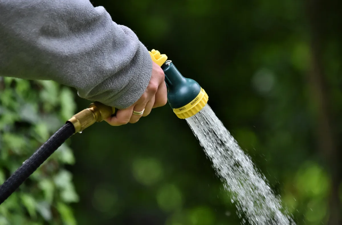 Man sieht eine Frau, die ihren Garten giesst.