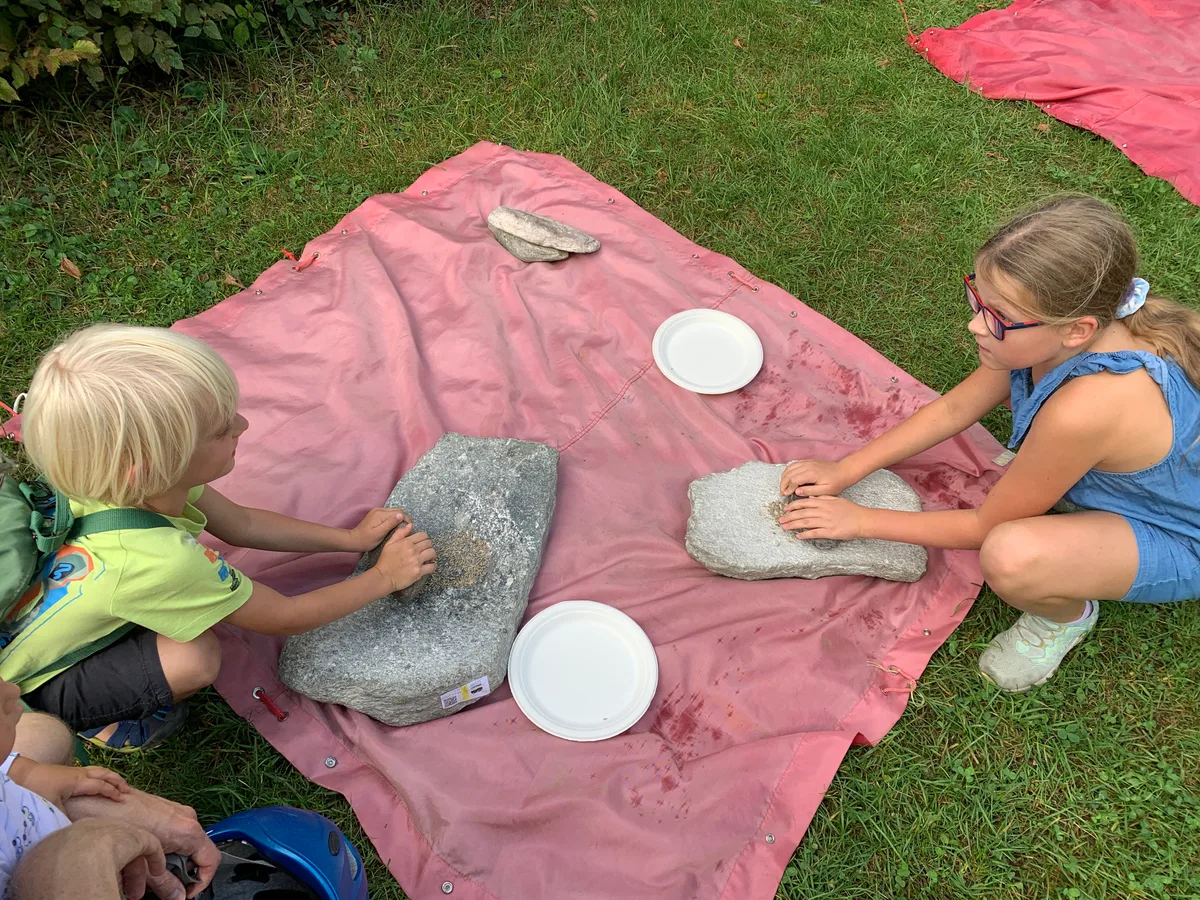 Kinder mahlen auf Steinen Körner.