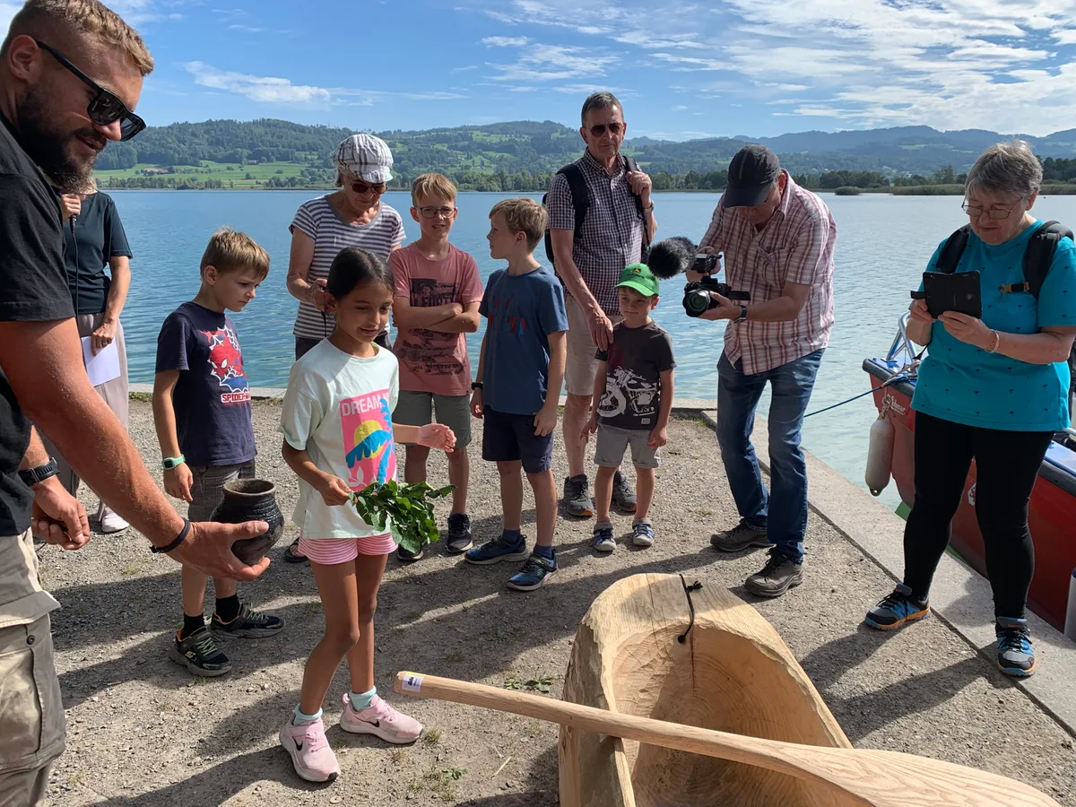 Kinder und Erwachsene stehen um einen Einbaum. 