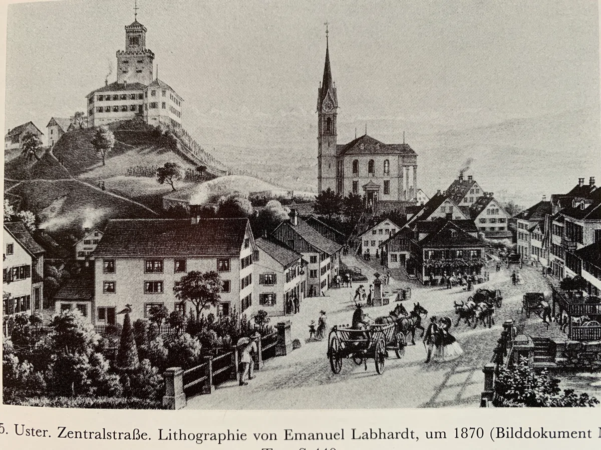 Eine historische Ansicht von Uster mit Burg und reformierter Kirche sowie Fuhrwerken auf der Zentralstrasse. Die Lithografie von Emanuel Labhardt entstand um 1870.