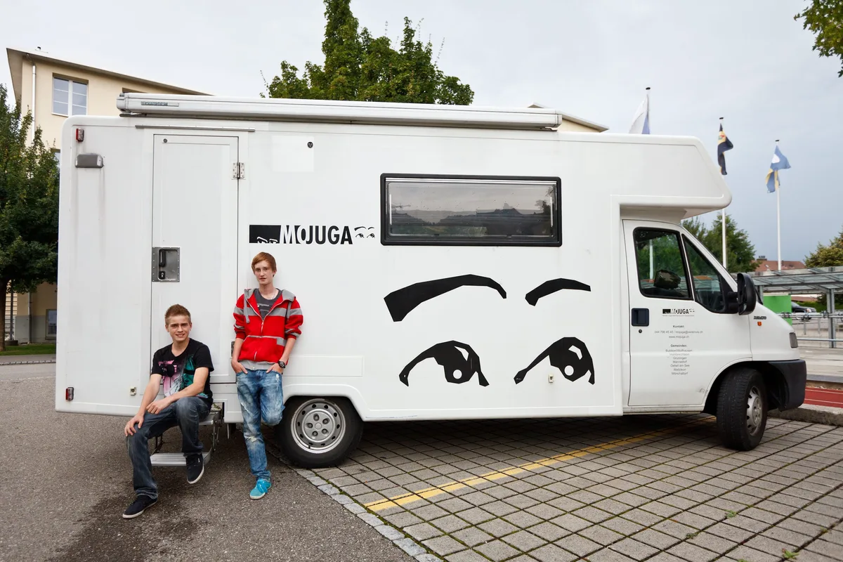 Zwei Jugendliche sitzen und stehen vor einem Wohnmobil.