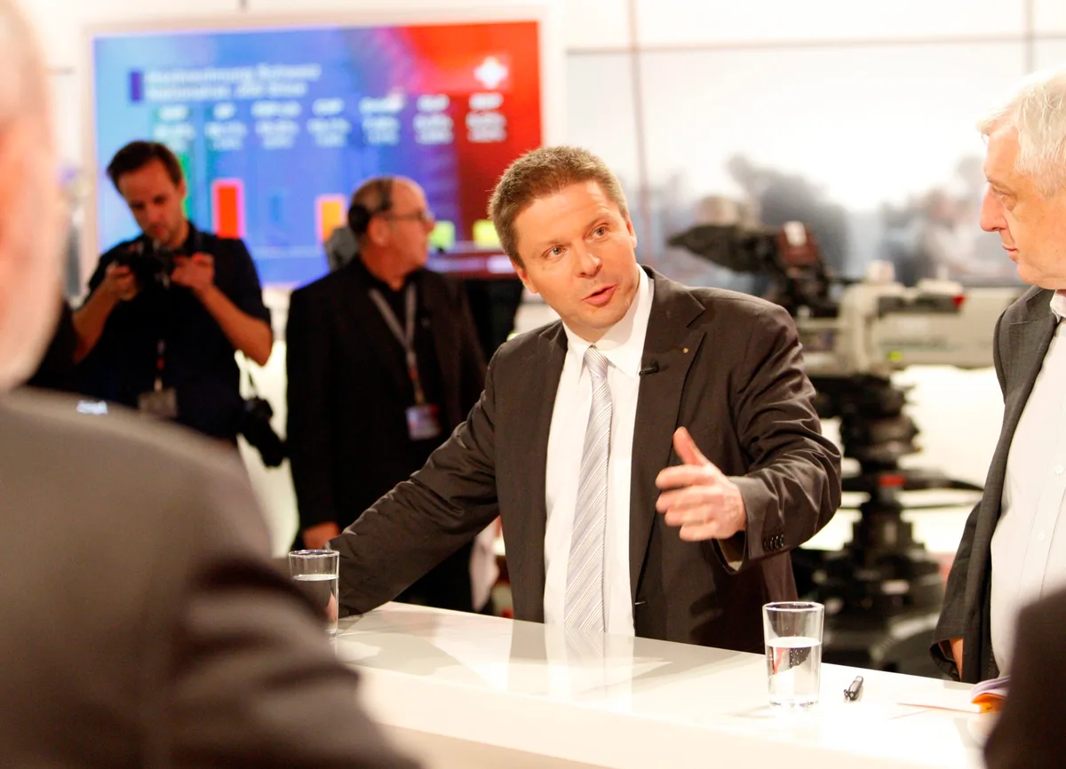 Ein Mann spricht an einem Stehtisch in einem Fernsehstudio.