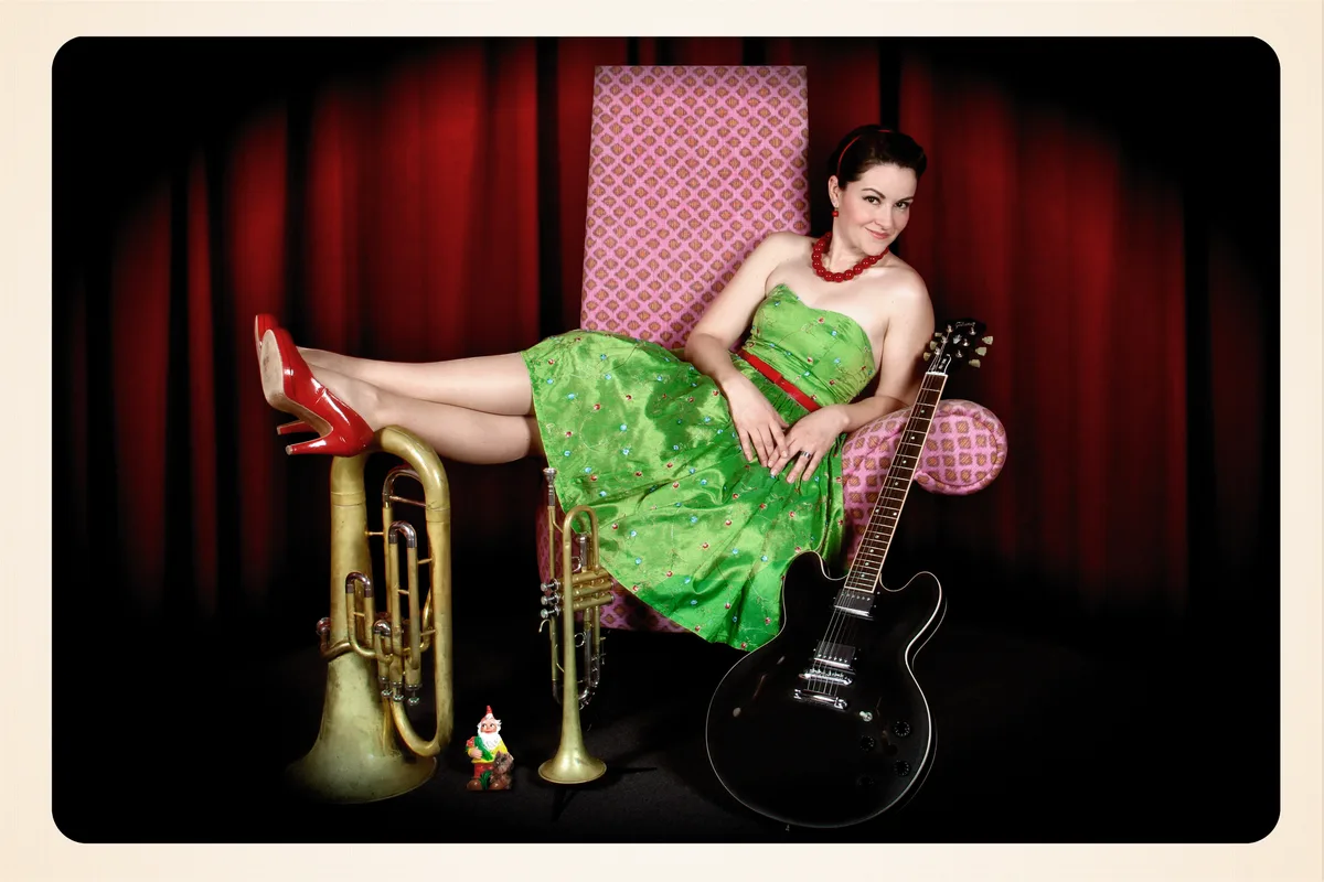 Frölein Da Capo tritt mit grünem Kleid, Tuba und Gitarre.