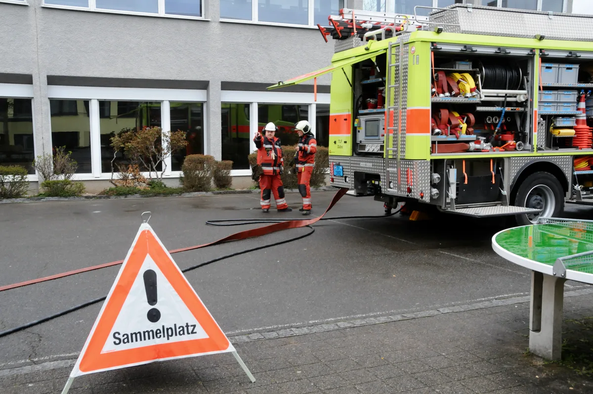 Man sieht Feuerwehr-Einsatzkräfte vor dem Schulhaus.