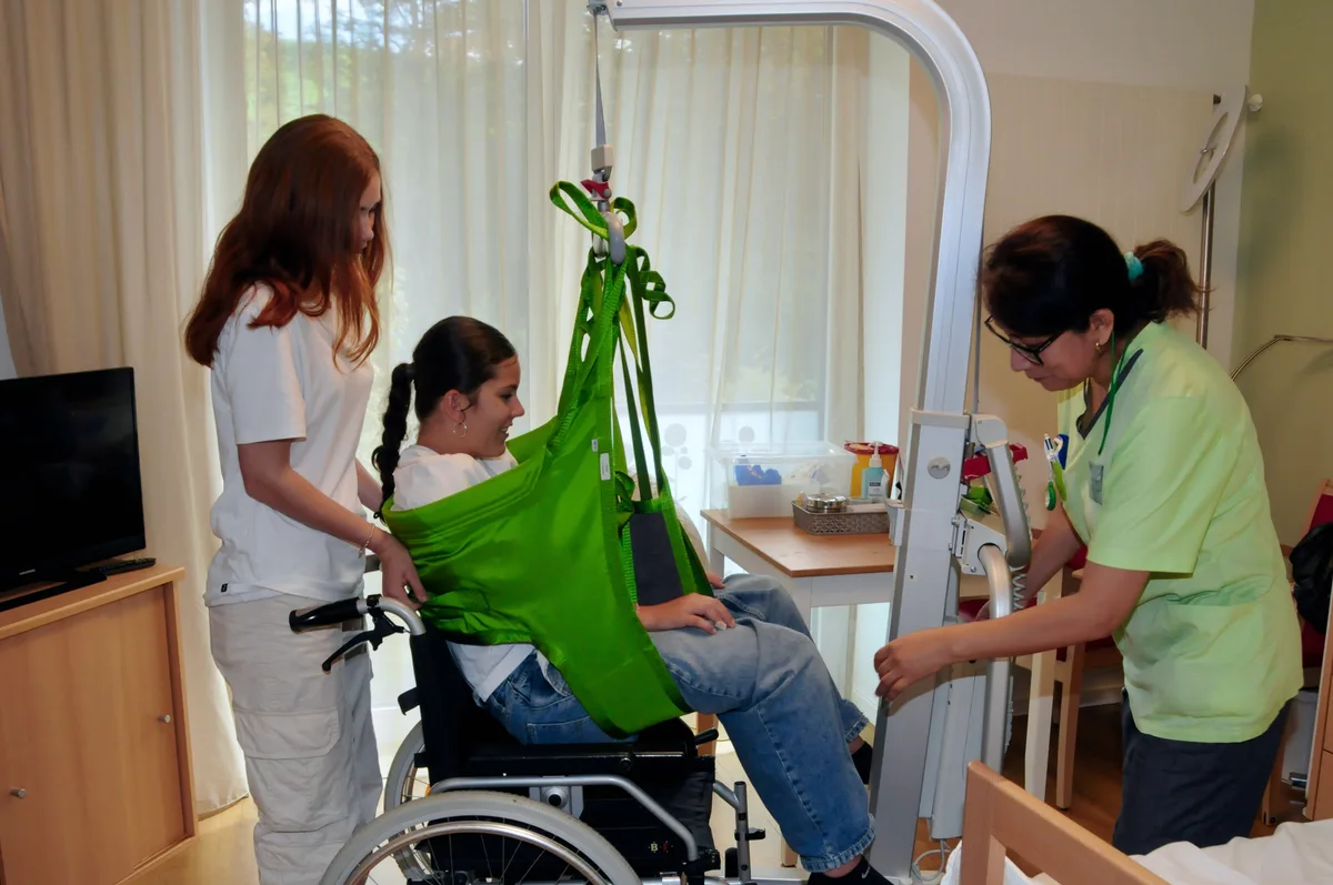 Man sieht Jugendliche unter Anleitung einer Pflegenden einen Patientenheber bedienen.